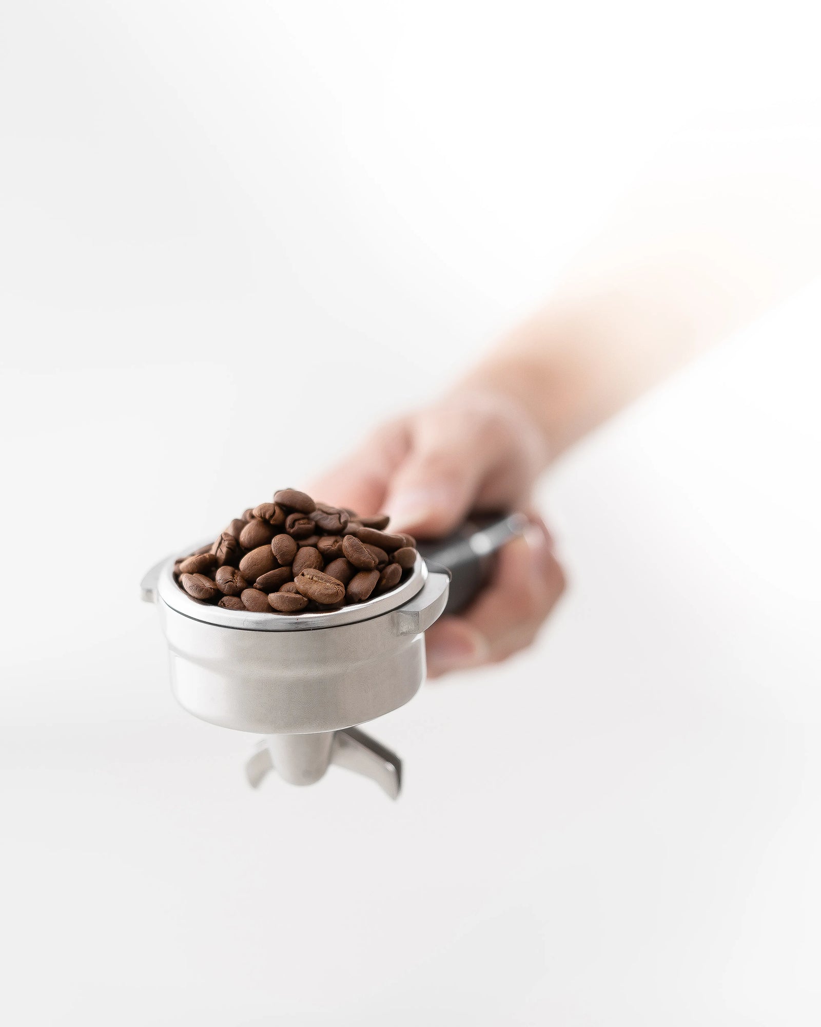 A portafilter basket filled with coffee beans about to be put into a coffee grinder